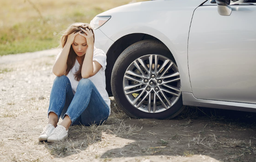 Worried woman sitting in the ground after a vehicle accident